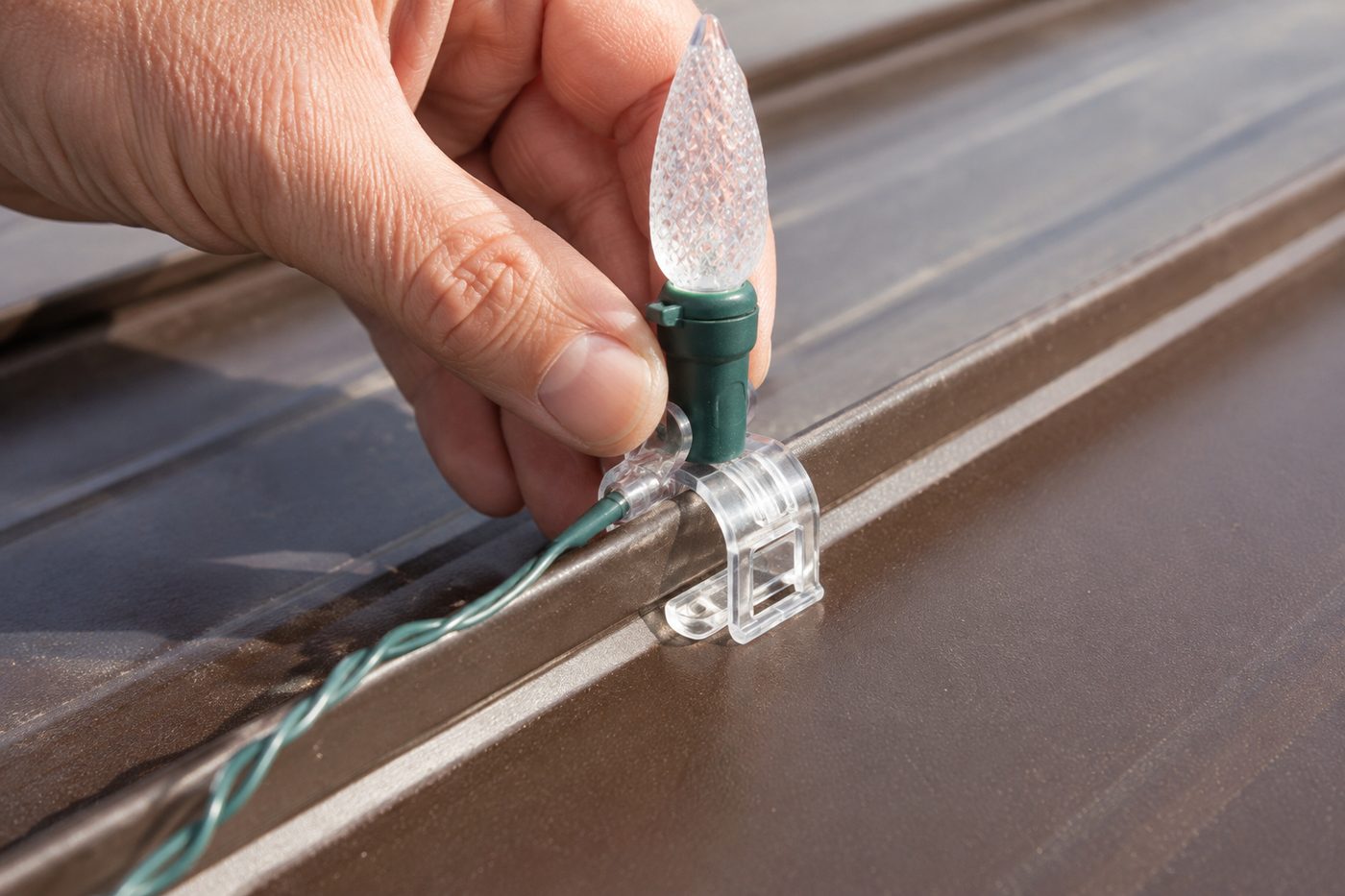 Hand clipping a C9 Christmas light socket onto a standing seam metal roof rib with a plastic clip