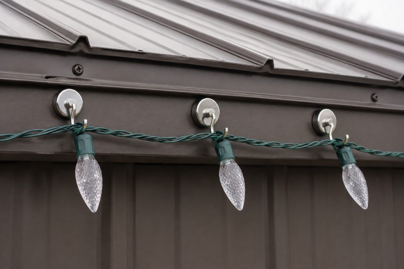 Magnetic hooks holding a strand of C9 Christmas lights along the steel eave trim of a metal building