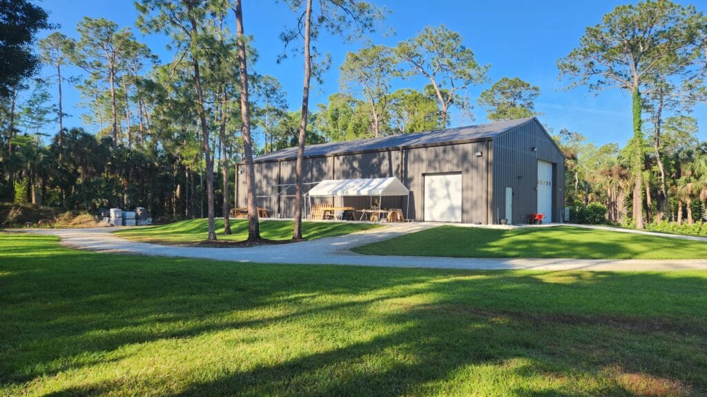 A barndominium surrounded by lush grass and trees. Depicts a barndominium for seasonal living.